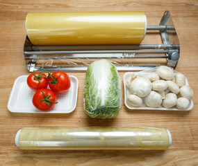 Rolls of transparent polyethylene food film for packing food on table with vegetables.