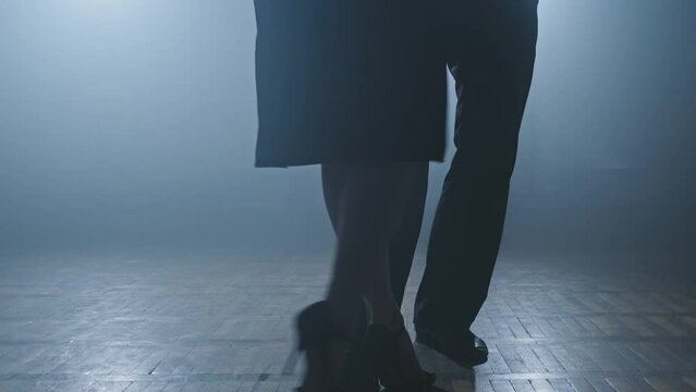 Legs of couple dancing tango in dark smoky studio in slow motion. Beautiful man and woman dancing latin dance. Close-up shot in 4K, UHD
