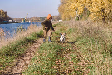 Kid playing with dog walking at rustic promenade along canal on nice Fall day