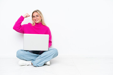 Young caucasian woman with laptop sitting on the floor doing strong gesture