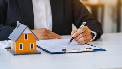 Real estate agent working sign agreement document contract for home loan insurance approving purchases for client with house model.