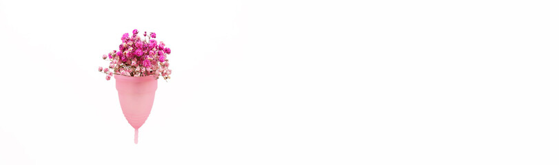 A pink menstrual cup made of medical silicone with a small bouquet of pink flowers levitates on a white background.  Isolate on white background.  Lots of empty space