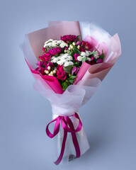 Bouquet of pink and white flowers wrapped in floral paper on a blue background.