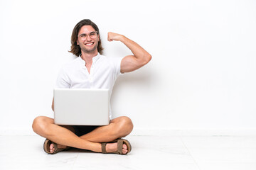 Young handsome man with a laptop sitting on the floor isolated on white background doing strong gesture