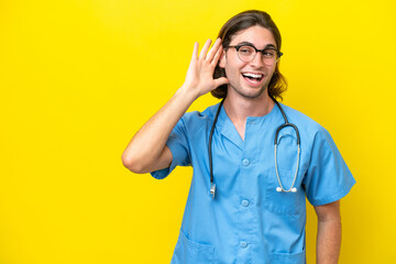 Young surgeon caucasian man isolated on yellow background listening to something by putting hand on the ear