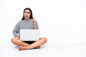 Young caucasian woman with a laptop sitting on the floor thinking an idea pointing the finger up