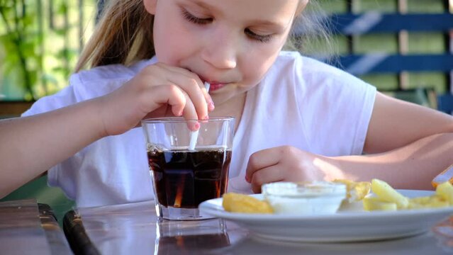 Child Pretty Girl  Drinking Cold Fizzy Beverage Cola From Glass Cup With Straw And Eating Chicken Nugget