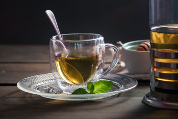 Herbal mint tea cup Transparent glass dark background wooden table still life honey bowl metal kettle teapot spoon cozy
