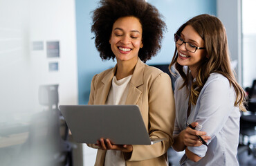 Happy multiethnic business women working together online on a laptop in corporate office.