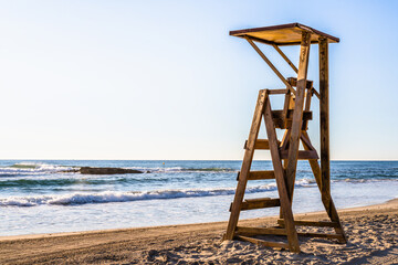 Mediterranean beach with wooden lifeguard chair in sunset time, in Spain. Teal and orange style.