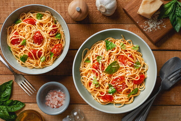 Plates of spaghetti with cherry tomatoes and fresh basil and ingredients on wooden background top...