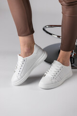 Close up of fashionable white sneakers on legs of girl on white background in studio.