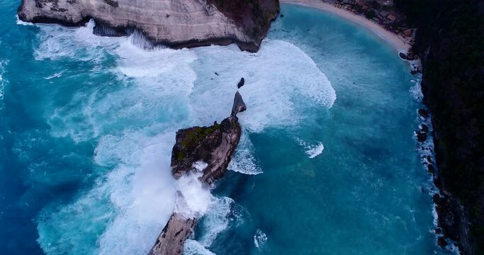 Aerial shot of bay with turquoise water, rocky cliffs with waves crashing