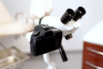 a modern microscope connected to a reflex camera against the background of a medical chair