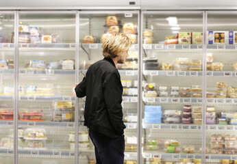  Man choosing frozen food from a supermarket freezer., reading product information