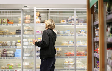  Man choosing frozen food from a supermarket freezer., reading product information