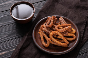 Homemade churros with chocolate on a dark wooden rustic background.