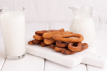 Homemade churros with milk and cream on a white wooden background.