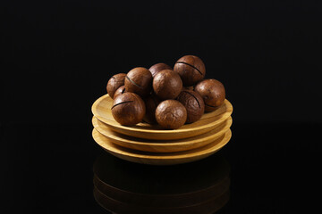 Macadamia nut on a stack of wooden plates on a dark table with reflection. Close-up