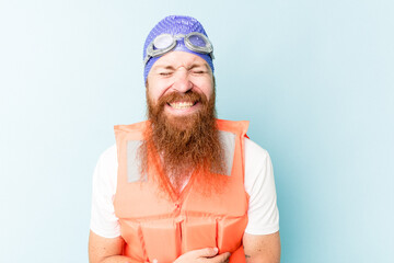 Young caucasian man wearing life jacket isolated on blue background laughing and having fun.