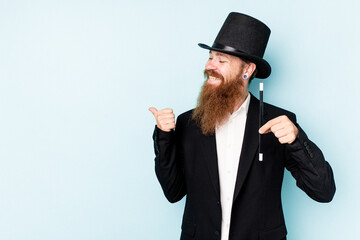 Young magician man isolated on blue background points with thumb finger away, laughing and carefree.
