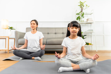 Fototapeta na wymiar Asian young mother and her daughter setting prepare to yoga and meditation pose together on yoga mat in living room at home. Fitness lifestyle.