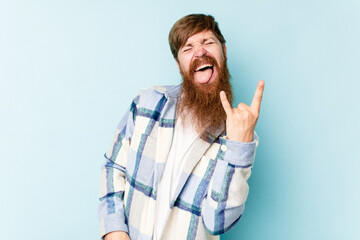 Fototapeta premium Young caucasian red-haired man isolated on blue background showing rock gesture with fingers