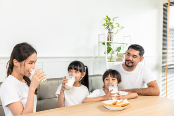 Asian  family enjoying breakfast at living room. little girl daughter sitting on table, drinking milk with smiling father and mother in morning. Happy family at home.