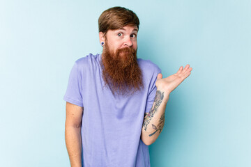 Young caucasian red-haired man isolated on blue background doubting and shrugging shoulders in...