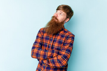 Young caucasian red-haired man isolated on blue background dreaming of achieving goals and purposes