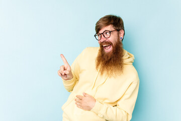 Young caucasian red-haired man isolated on blue background looks aside smiling, cheerful and pleasant.