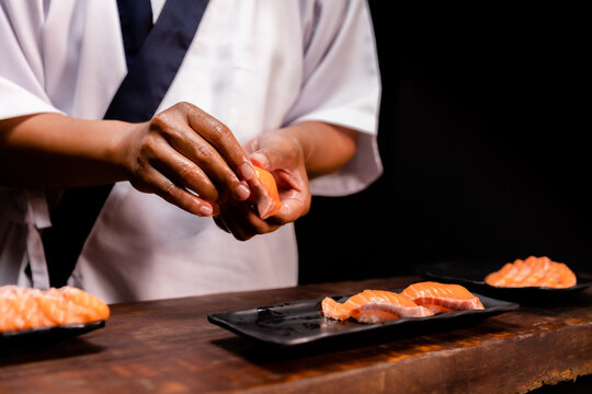 Chef's hand holding fresh piece of salmon.Closeup of chef hands preparing japanese food. Japanese chef making sushi at restaurant.Chef making traditional japanese sushi on wood board.