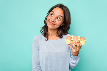 Young hispanic woman holding eggs isolated on blue background dreaming of achieving goals and purposes