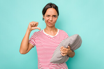Young hispanic woman holding a cushion isolated on white background showing a dislike gesture,...