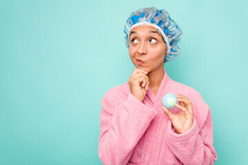 Young hispanic woman holding bathtub ball isolated on blue background looking sideways with...