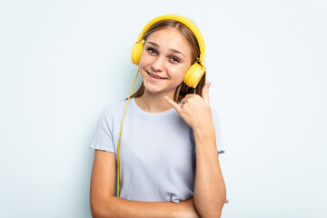 Young caucasian girl listening to music isolated on blue background showing a mobile phone call gesture with fingers.