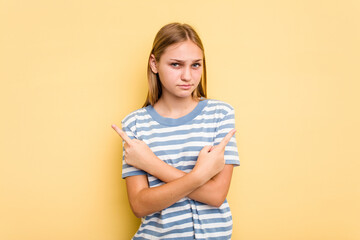 Young caucasian girl isolated on yellow background points sideways, is trying to choose between two options.