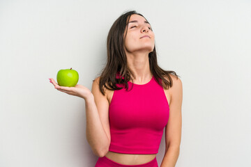 Young caucasian woman holding an apple isolated on white background dreaming of achieving goals and purposes