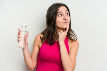 Young caucasian woman holding a bottle of water isolated on white background relaxed thinking about something looking at a copy space.