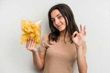 Young caucasian woman holding crisps isolated on yellow background cheerful and confident showing...