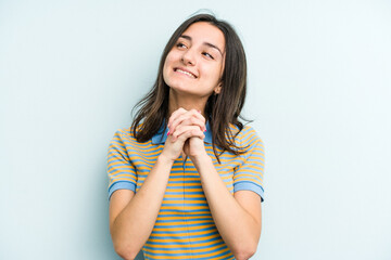 Young caucasian woman isolated on blue background keeps hands under chin, is looking happily aside.
