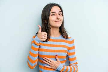 Fototapeta premium Young caucasian woman isolated on blue background touches tummy, smiles gently, eating and satisfaction concept.