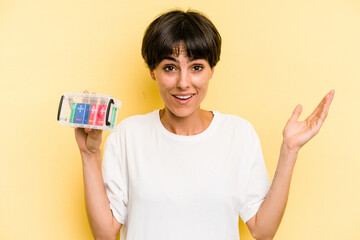 Young caucasian woman holding a batteries box isolated on yellow background receiving a pleasant...