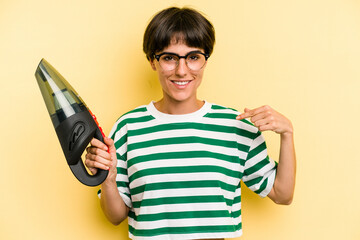 Young caucasian woman holding a hand vacuum cleaner isolated on yellow background person pointing...