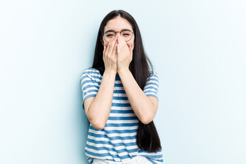 Young caucasian woman isolated on blue background laughing about something, covering mouth with hands.