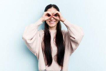 Young caucasian woman isolated on blue background showing okay sign over eyes