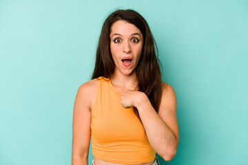 Young caucasian woman isolated on blue background surprised pointing with finger, smiling broadly.