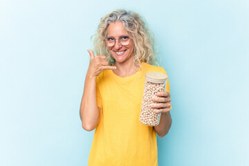 Middle age caucasian woman holding a chickpeas jar isolated on blue background showing a mobile phone call gesture with fingers.