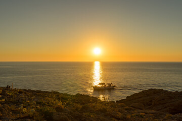 A pleasure craft breaks through the sunset reflected on the sea