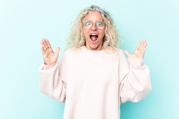 Middle age caucasian woman isolated on blue background receiving a pleasant surprise, excited and raising hands.